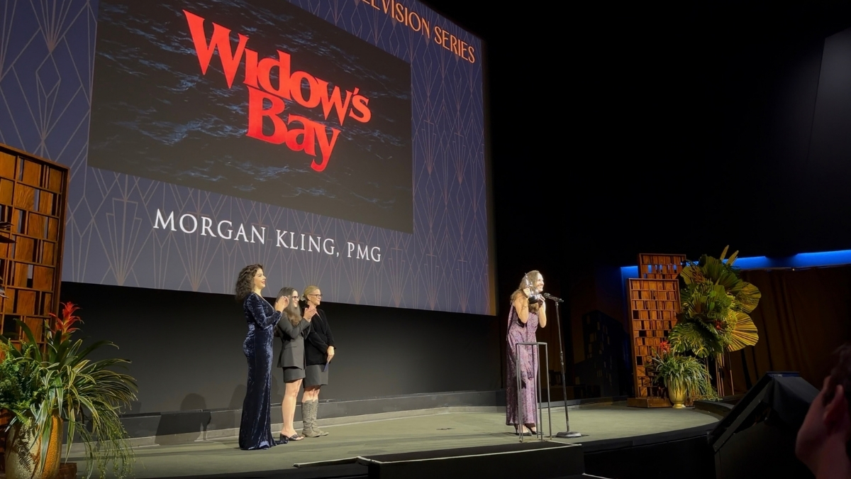 Morgan Kling holds a MacGuffin Award onstage beneath the Widow’s Bay presentation screen