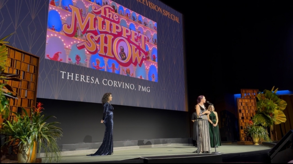 Theresa Corvino speaks onstage beneath The Muppet Show presentation screen.